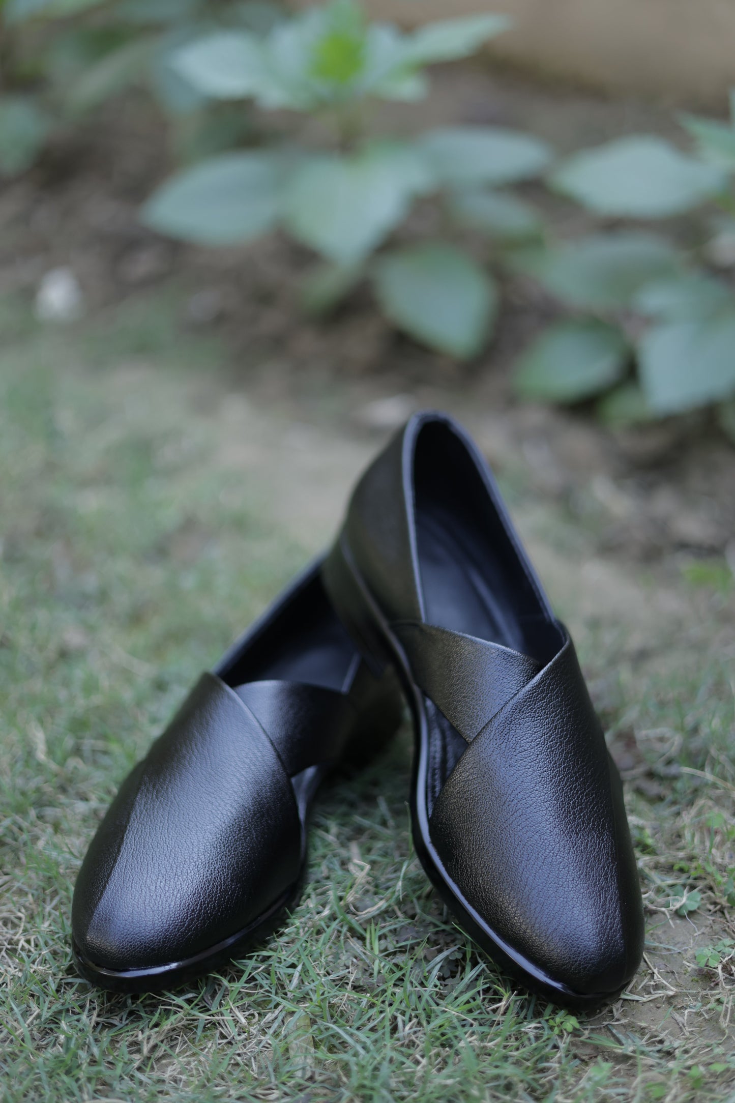 Pair of black leather shoes on grass with blurred green leaves in the background