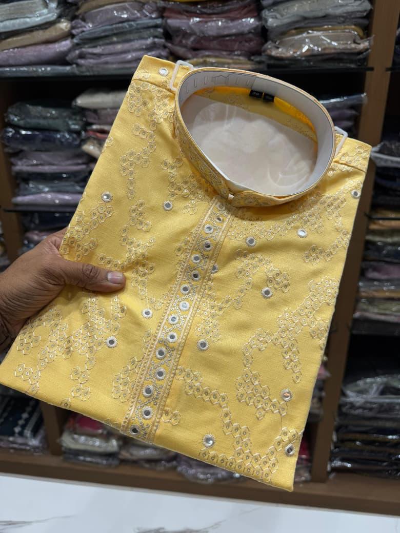 Yellow embroidered garment held by a hand with a background of folded fabric.