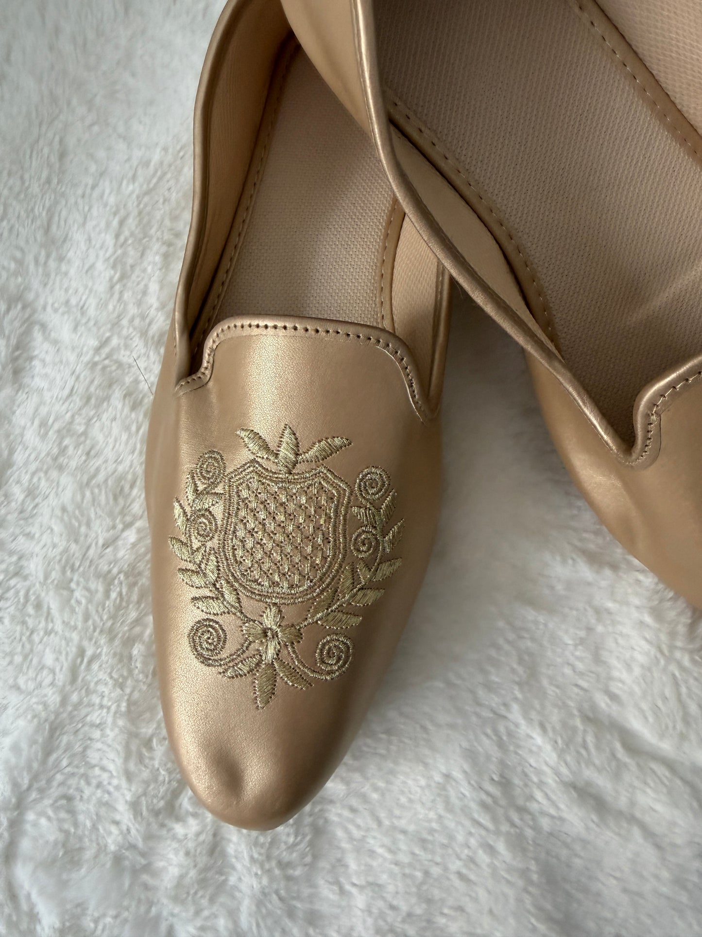 Gold loafer with intricate embroidery on a white textured surface
