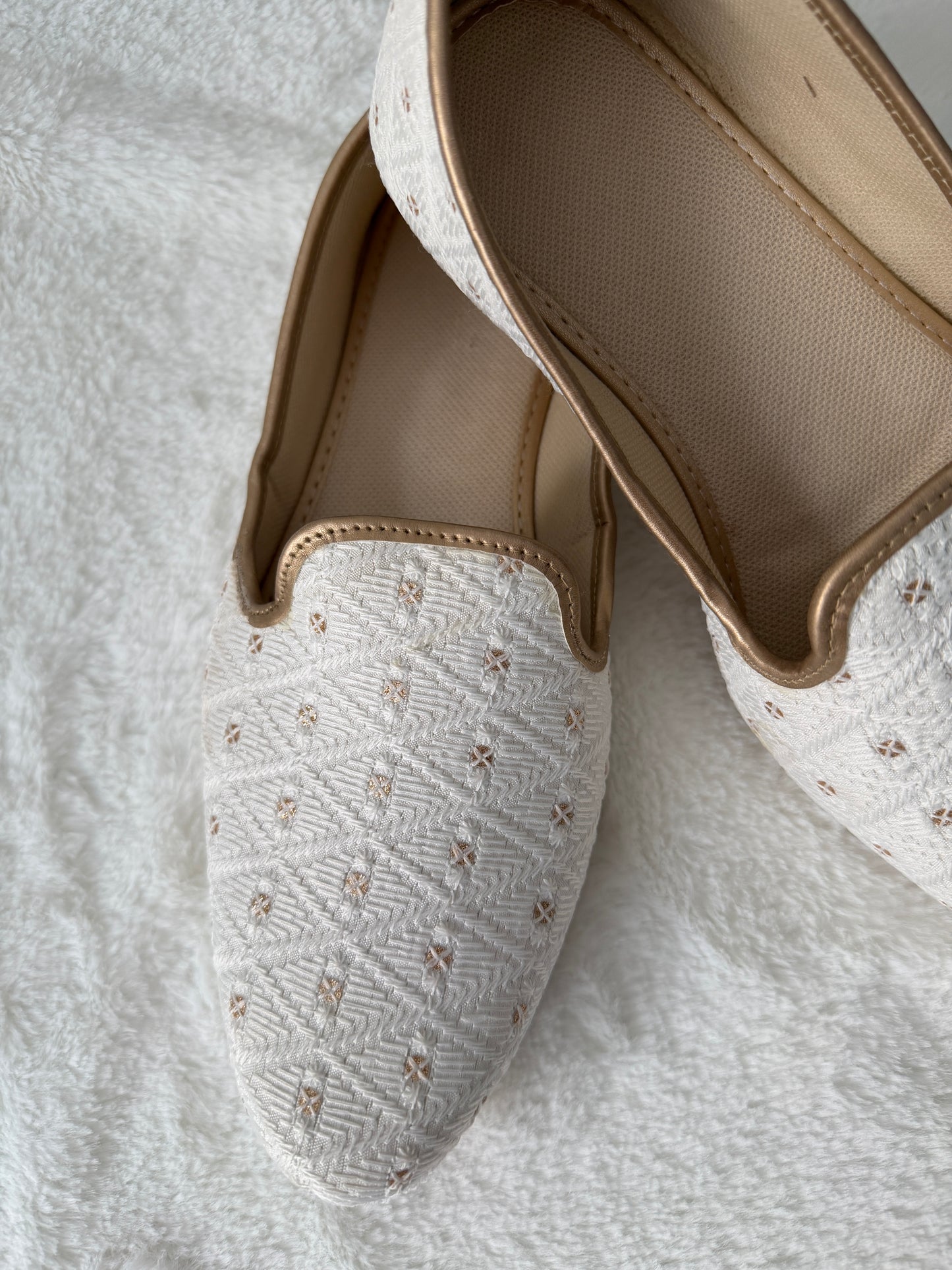 Pair of white embroidered slippers on a light gray background