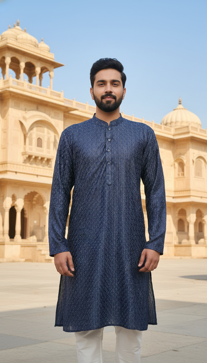 Man wearing a blue kurta with white pants in front of an architectural building.