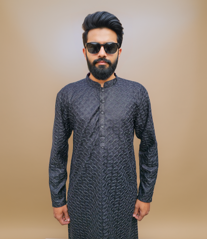 Man wearing a dark patterned kurta against a beige background
