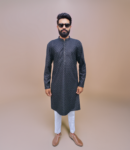 Man wearing a dark patterned kurta with metallic shine with white pants on a beige background