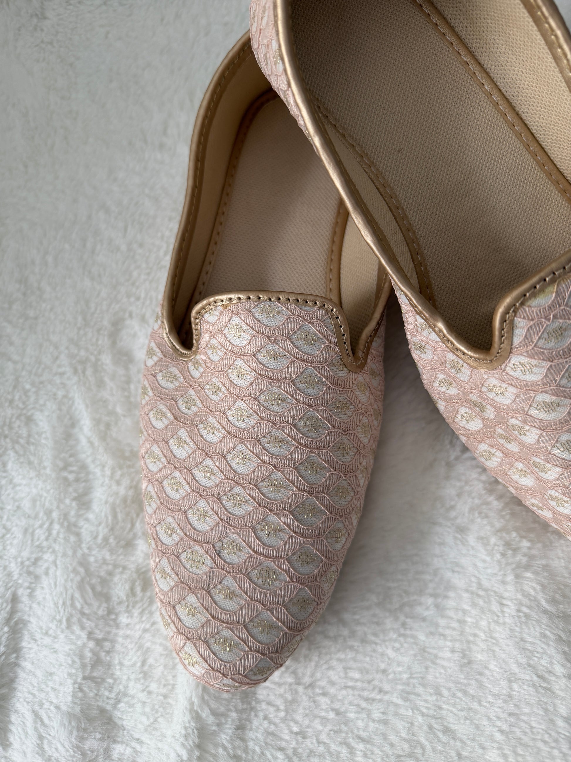 Close-up of a pink jutti with lace detailing on a textured white surface