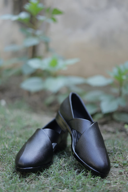 Pair of black jutti on a textured surface with blurred greenery in the background