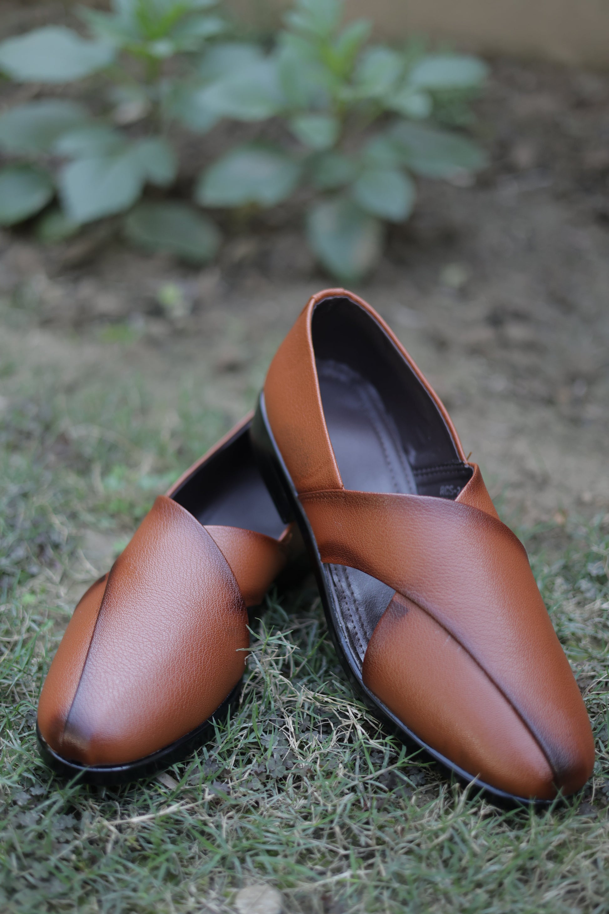 Pair of brown leather jutti on a textured surface with greenery