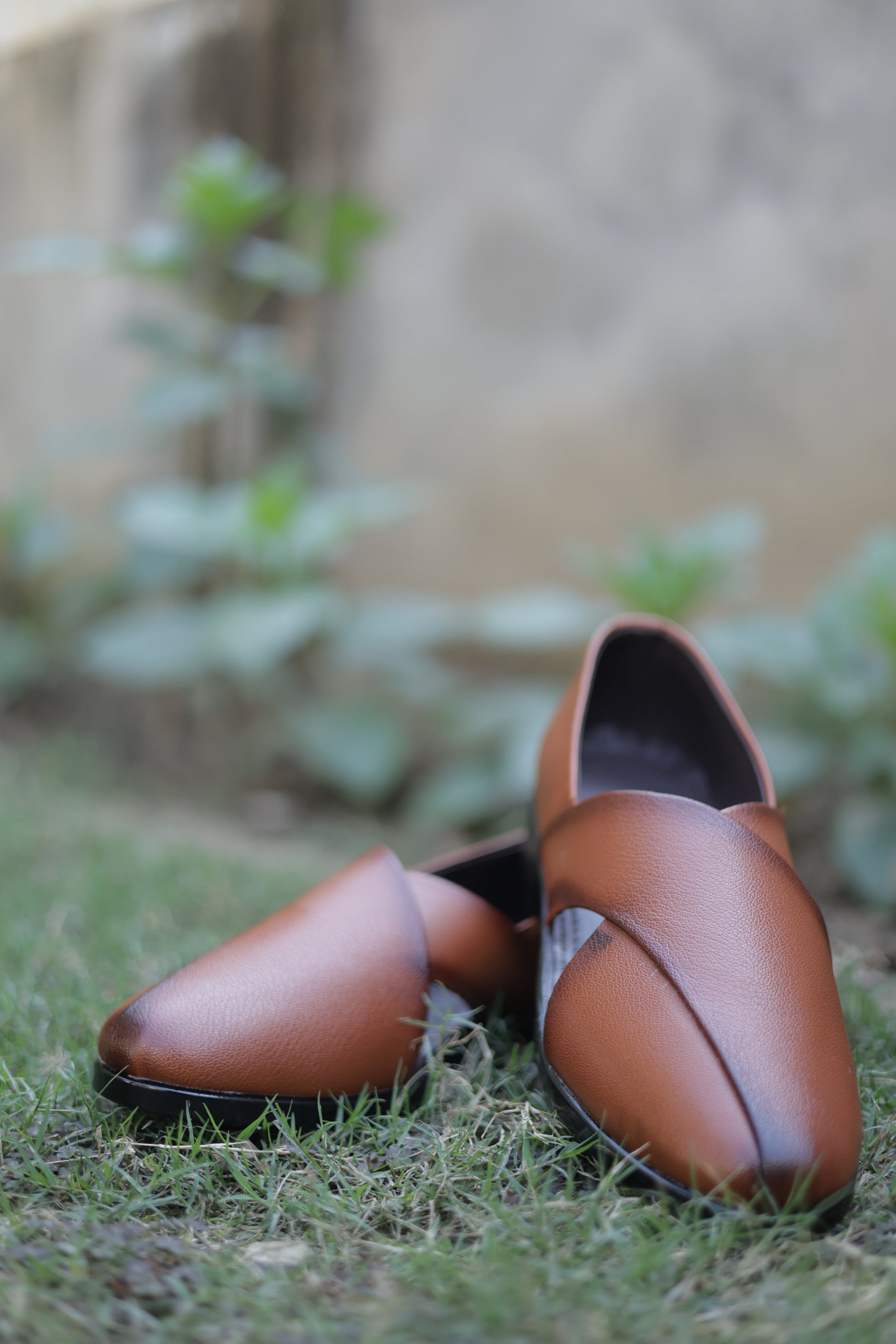 Pair of brown leather jutti on a textured surface with a blurred natural background