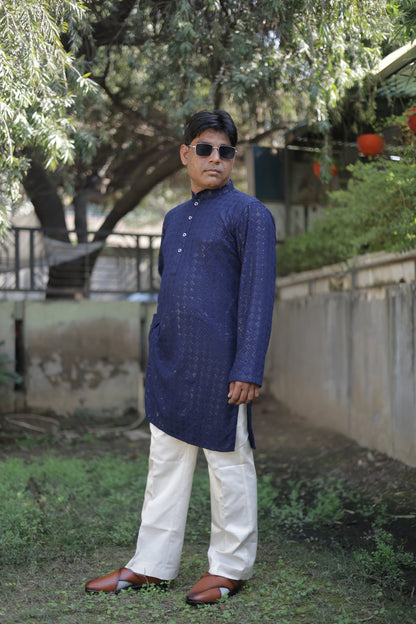Person wearing a blue kurta and sunglasses standing on a path with greenery around