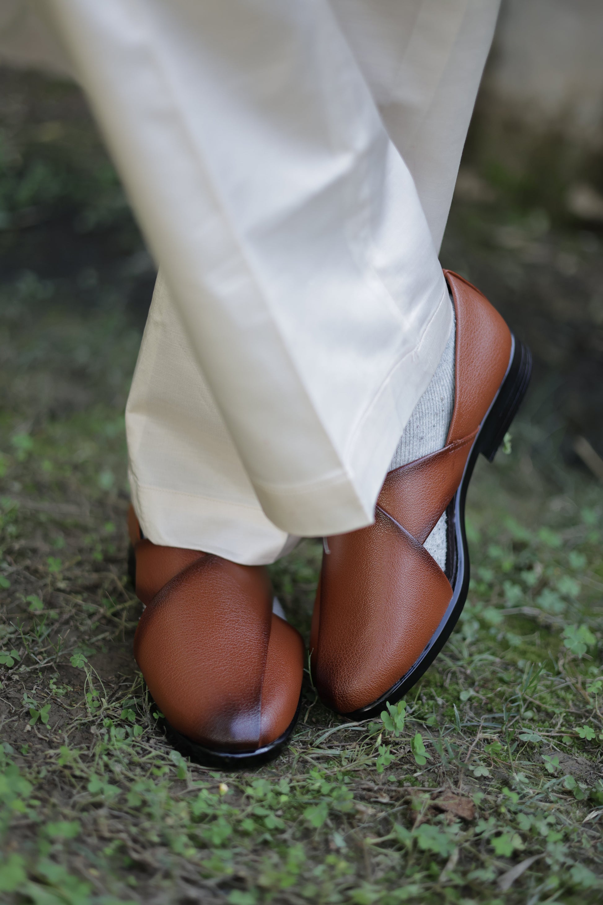 Brown jutti and beige pants on a green grass background