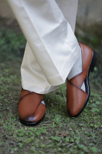 Brown jutti and light-colored pants on a grassy ground