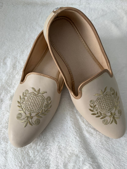 Pair of beige jutti with floral embroidery on a white fabric background