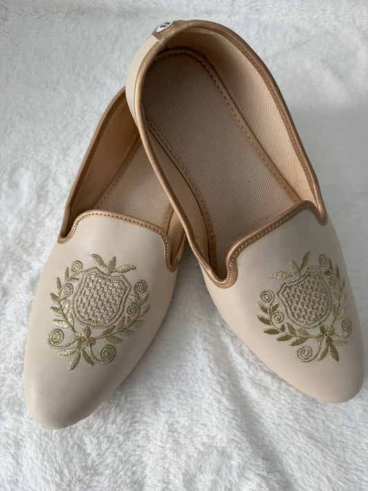 Pair of beige jutti with floral embroidery on a white fabric background