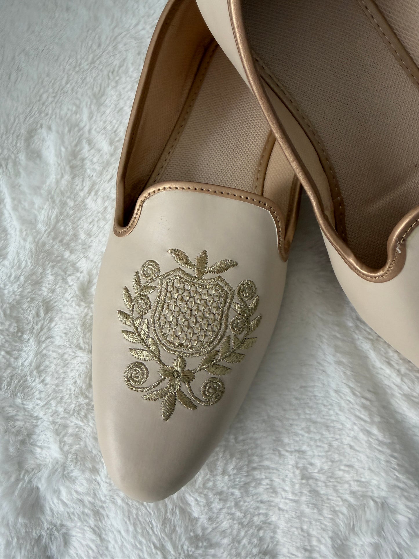 Beige jutti with intricate design on a textured white background