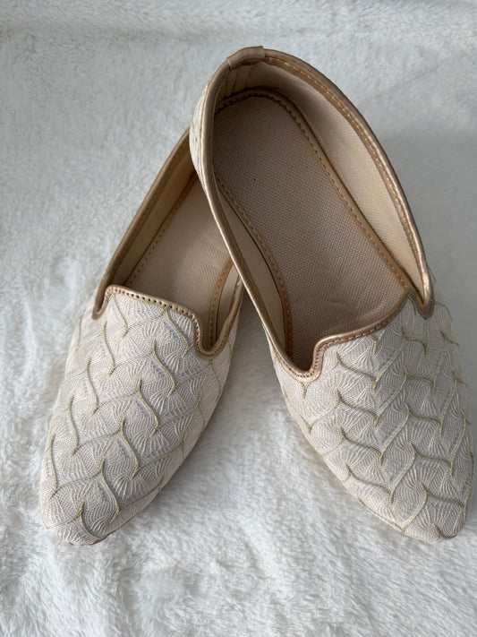 Pair of beige slip-on shoes with textured sole on a light gray background