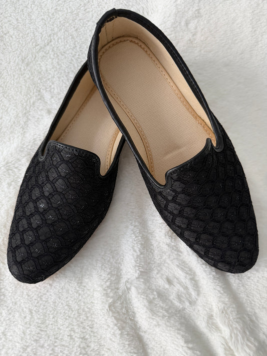 Black textured loafers/jutti on a white textured surface