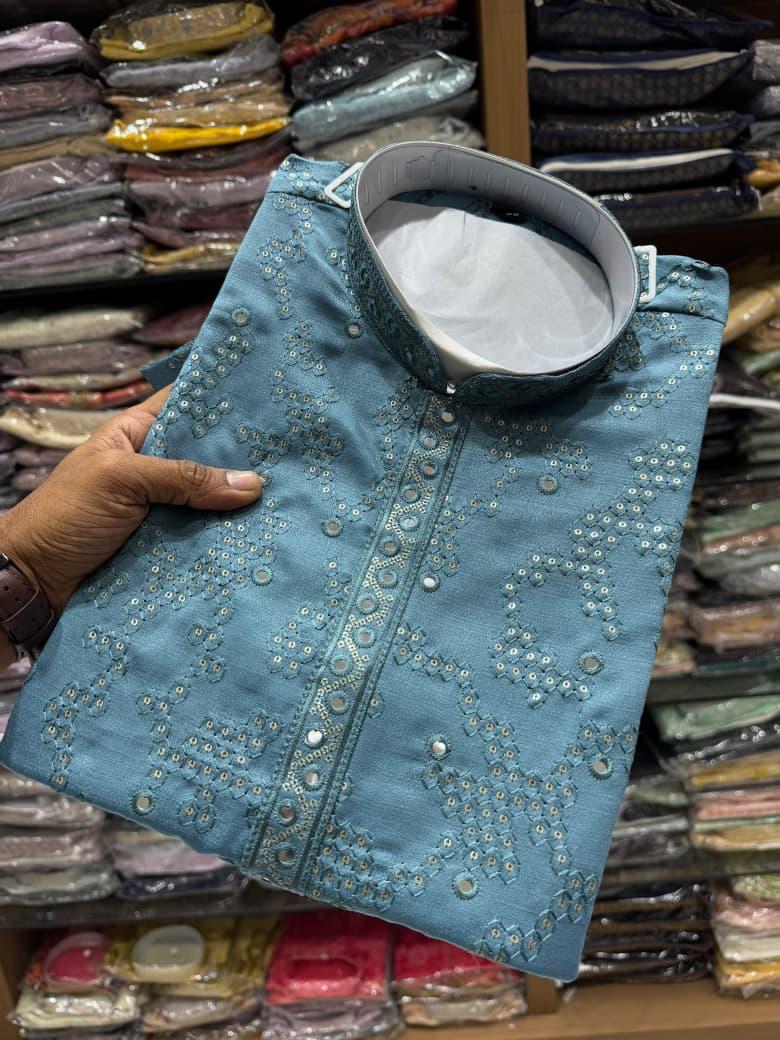 Blue kurta held by a hand with a background of shelves with folded fabrics.