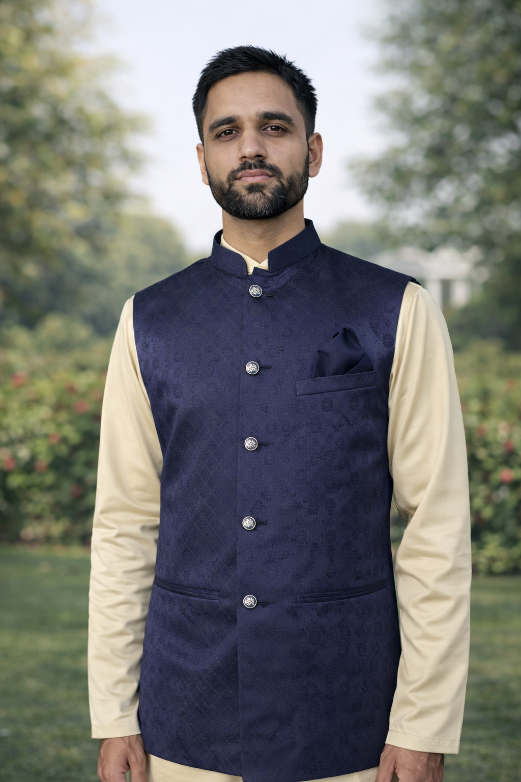 Man wearing a navy blue vest over a cream shirt with a blurred natural background