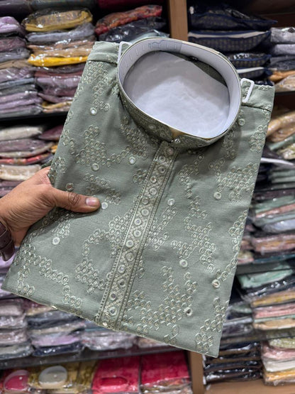 Green Kurta fabric held by a hand with a background of stacked fabrics.