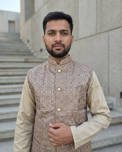 Man wearing a patterned vest over a beige shirt standing outdoors.