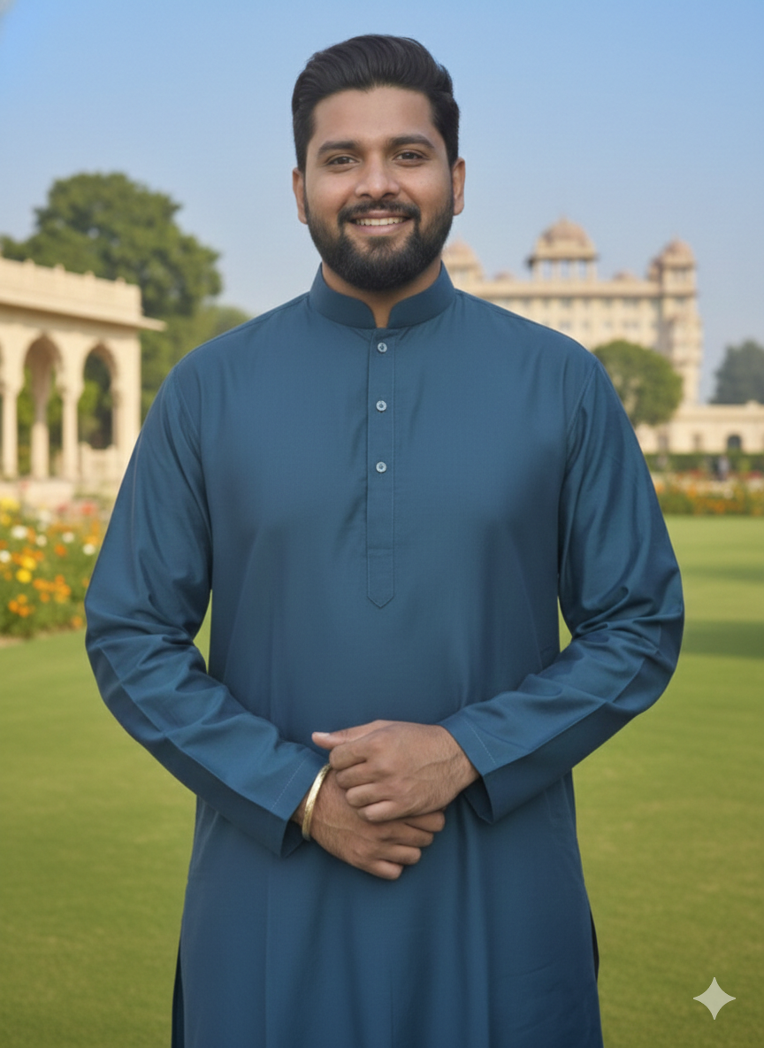 Man wearing a teal blue kurta standing in a garden with a building in the background