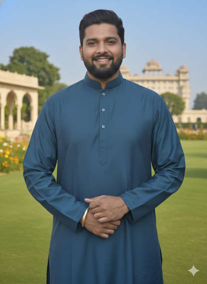 Man wearing a teal blue kurta standing in a garden with a building in the background