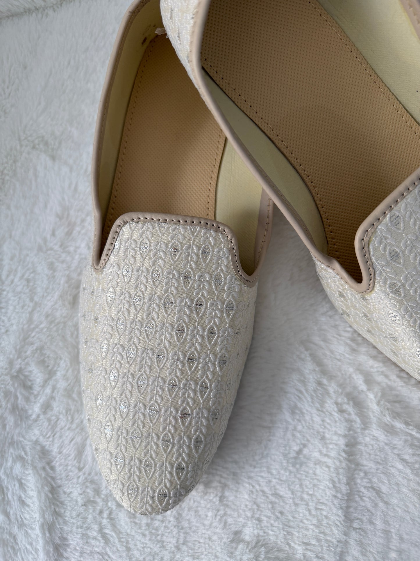 Pair of White Jutti with textured pattern on a white fabric background