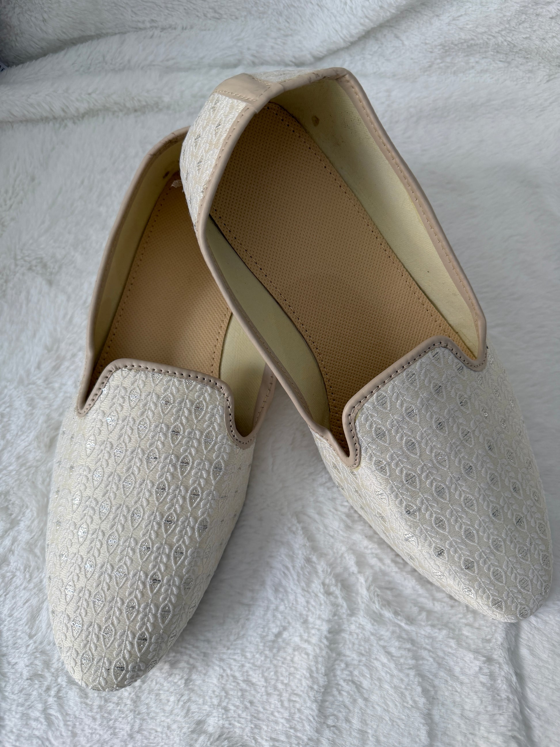 Pair of white jutti with textured pattern on a light gray background