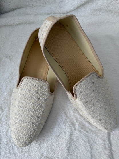 Pair of white jutti with textured pattern on a light gray background